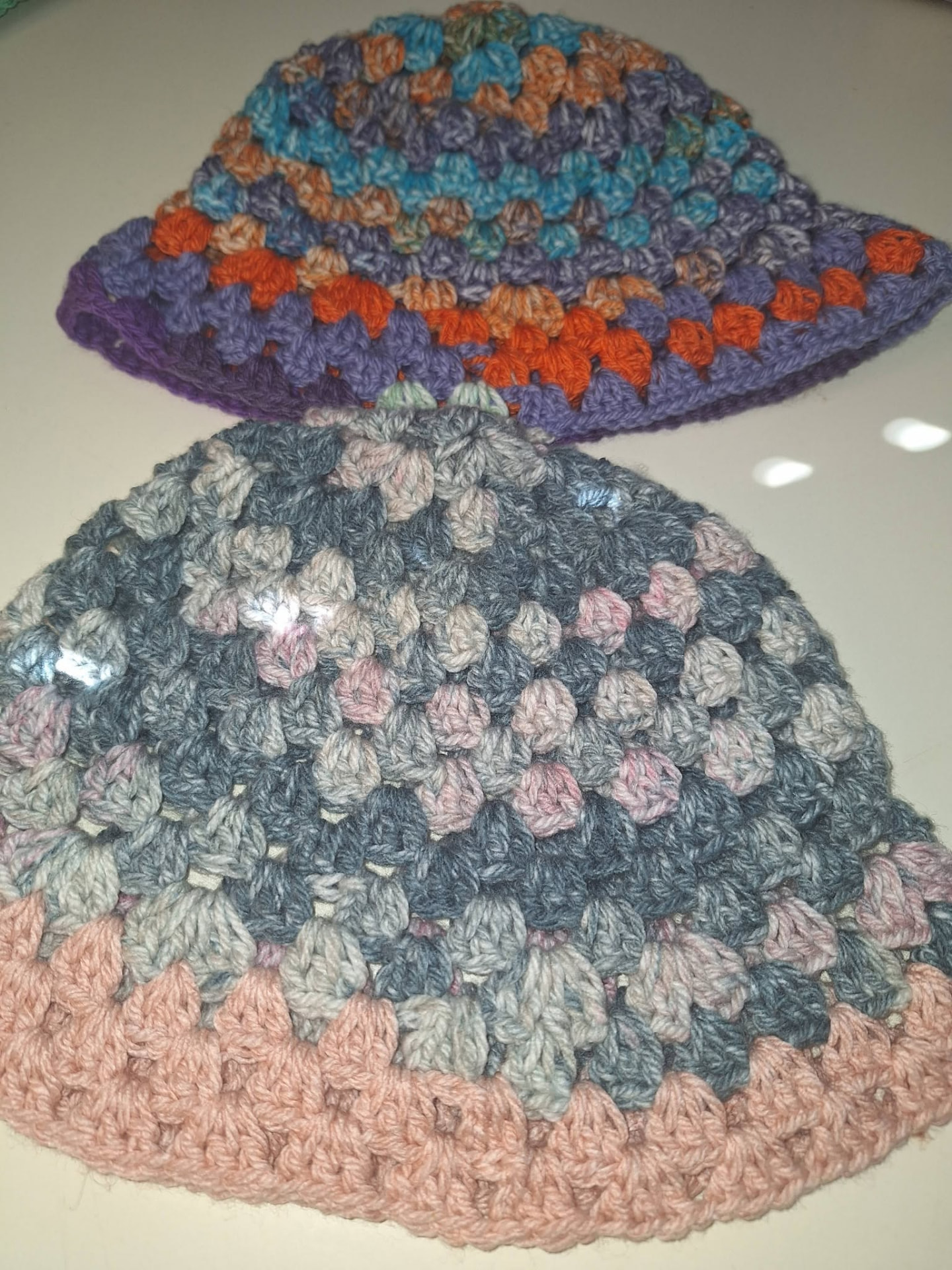 Two crochet bucket hats in purple-orange and grey-pink yarn